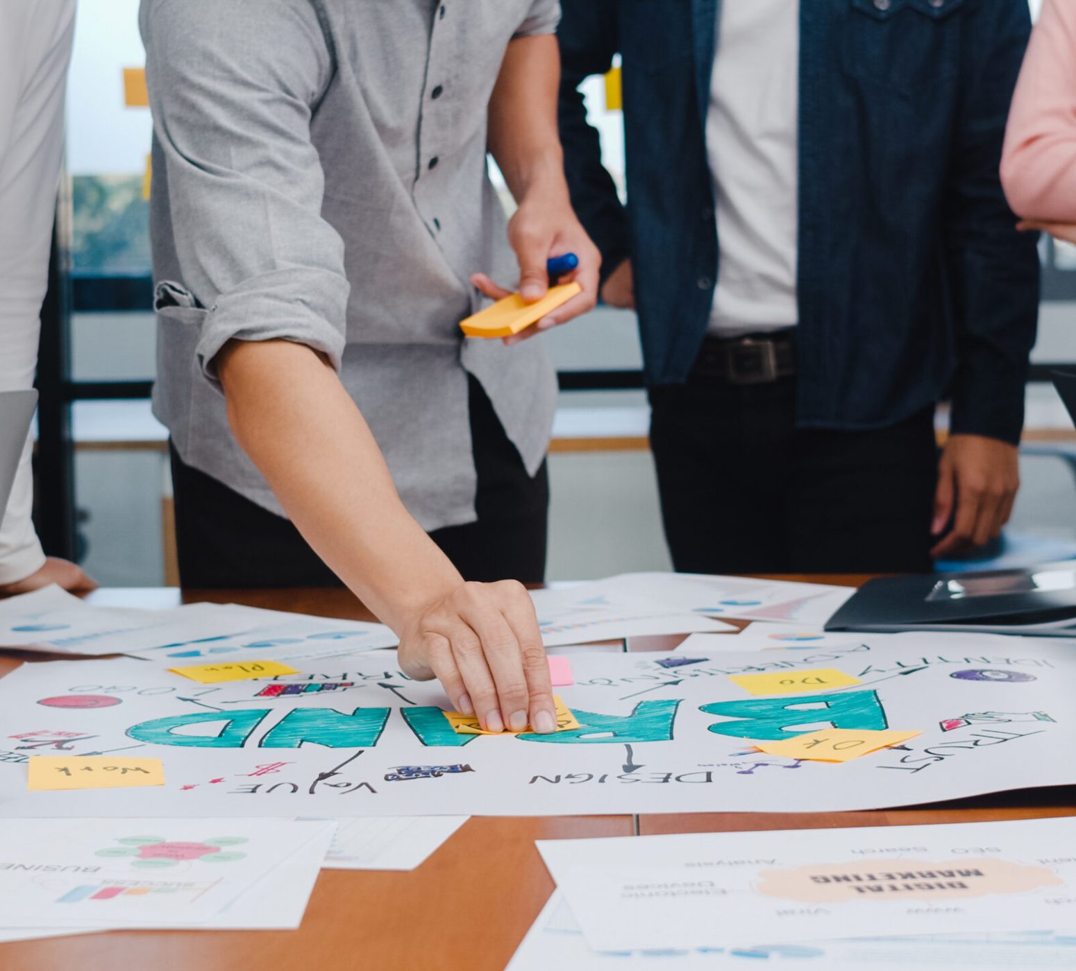 Happy young Asian businessmen and businesswomen meeting brainstorming ideas about new paperwork project colleagues working together planning success strategy enjoy teamwork in small modern office.